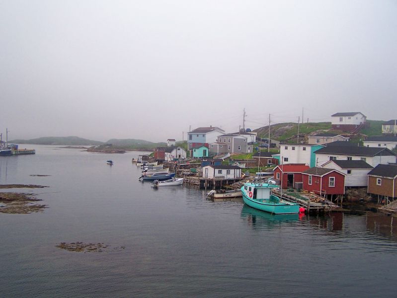 Photo of misty coast with a few small buildings and many small fishing boats