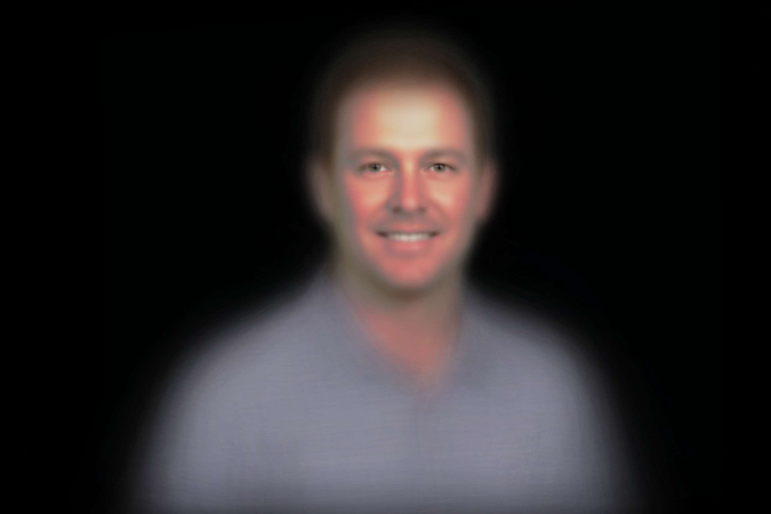 Generated image of a generic middle-aged white man in front of a black background looking at the camera. His eyes are in sharp focus, other parts of his face are blurry, and everything besides his face is very blurry.