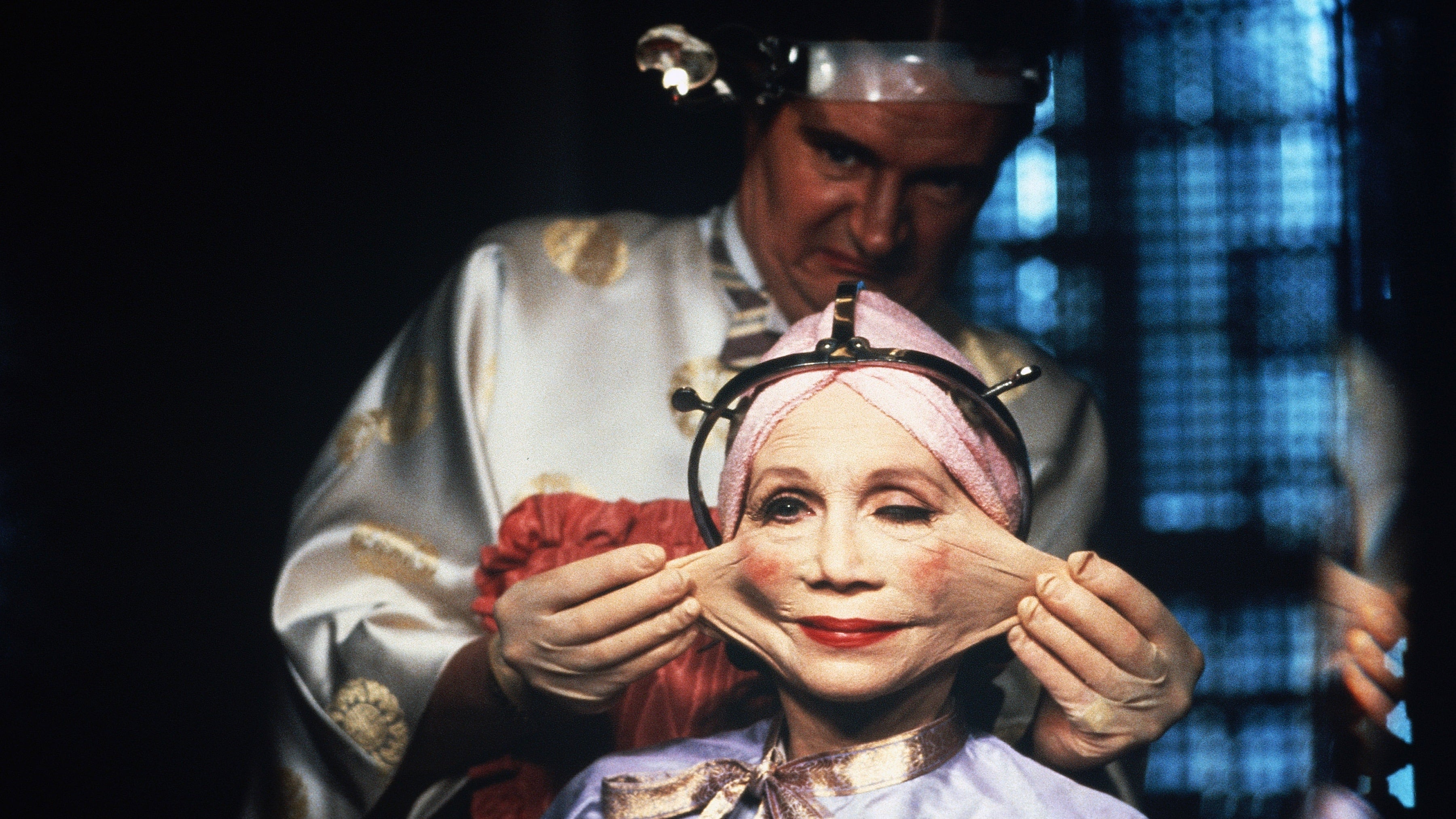 Image of a doctor standing behind a woman making a slightly disgusted look as he stretches the skin from her face out grotesquely