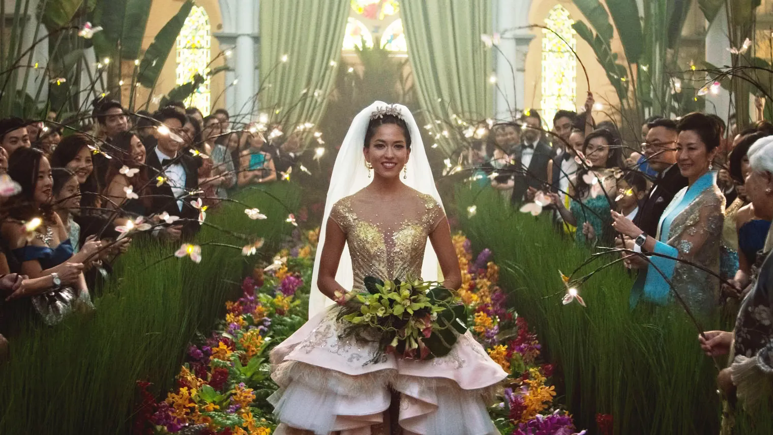 A bride walks down an elaborate wedding aisle surrounded by  tall live grass. All of the attendees have illuminated butterfly puppets extended.
