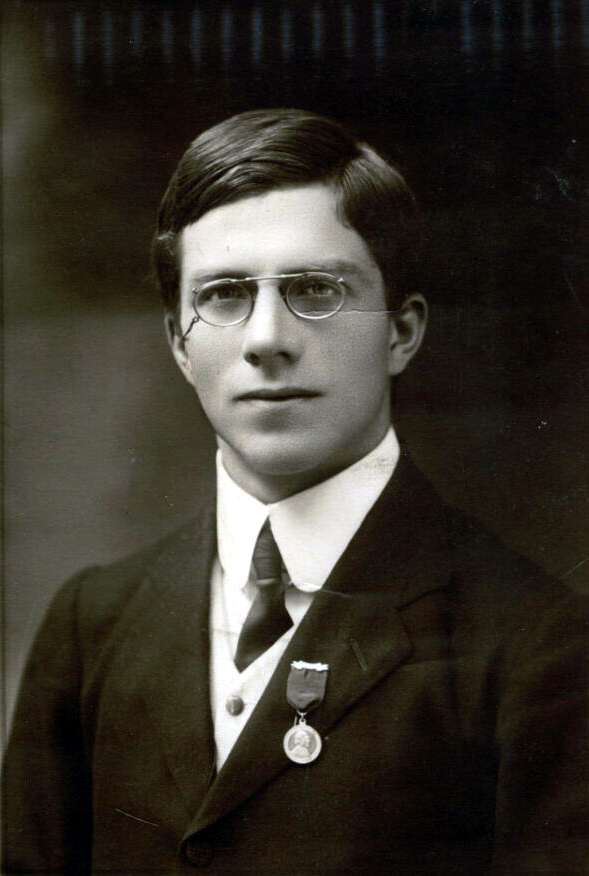 sepia photographic portrait of a young, early-20th-century elite man. He has specatactles and some sort of medal pinned to his chest.