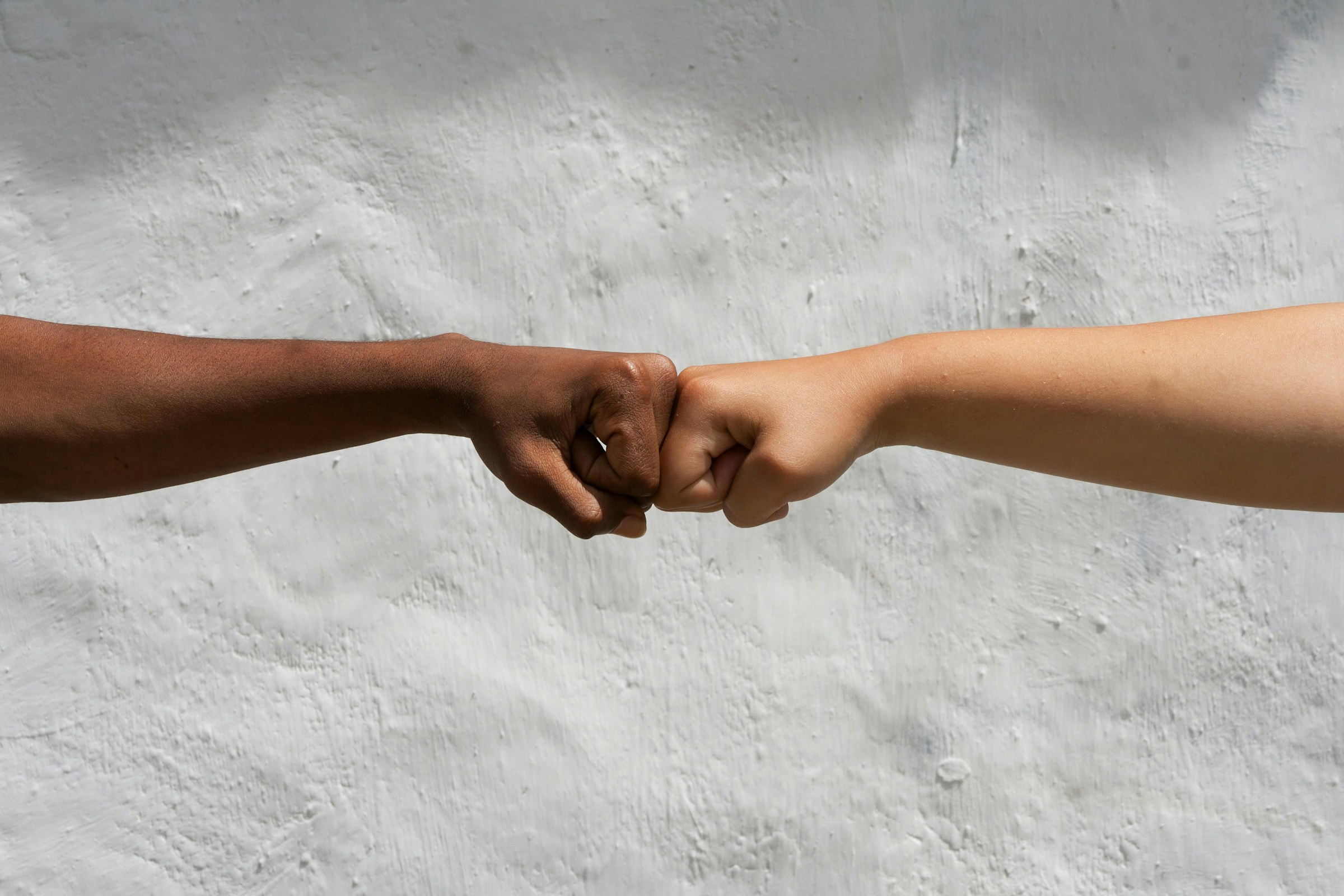 Photo of two fists bumping in greeting in front of a white textured background