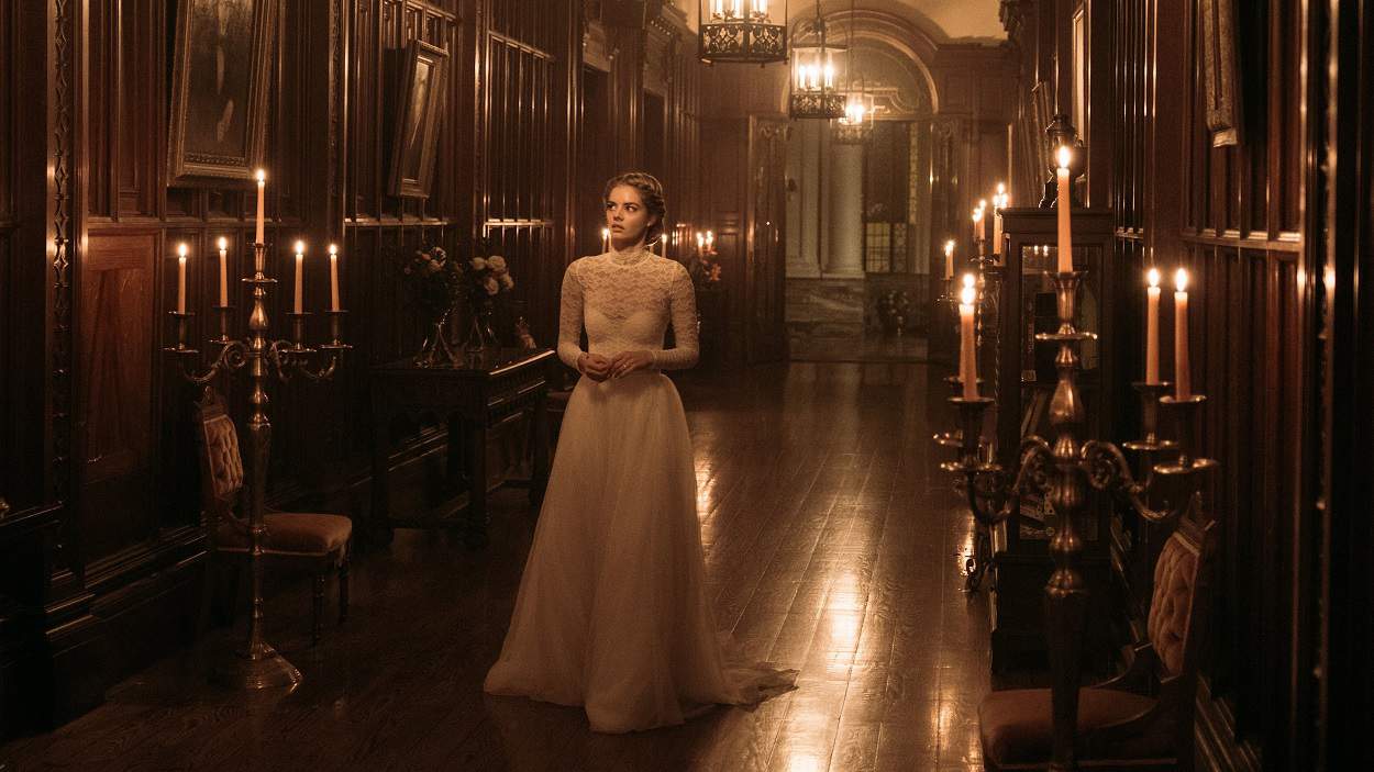 Movie still (Ready or Not, 2019). A woman in a white wedding dress walks down a slightly creepy, candle-lit hallway in a lavish old house.