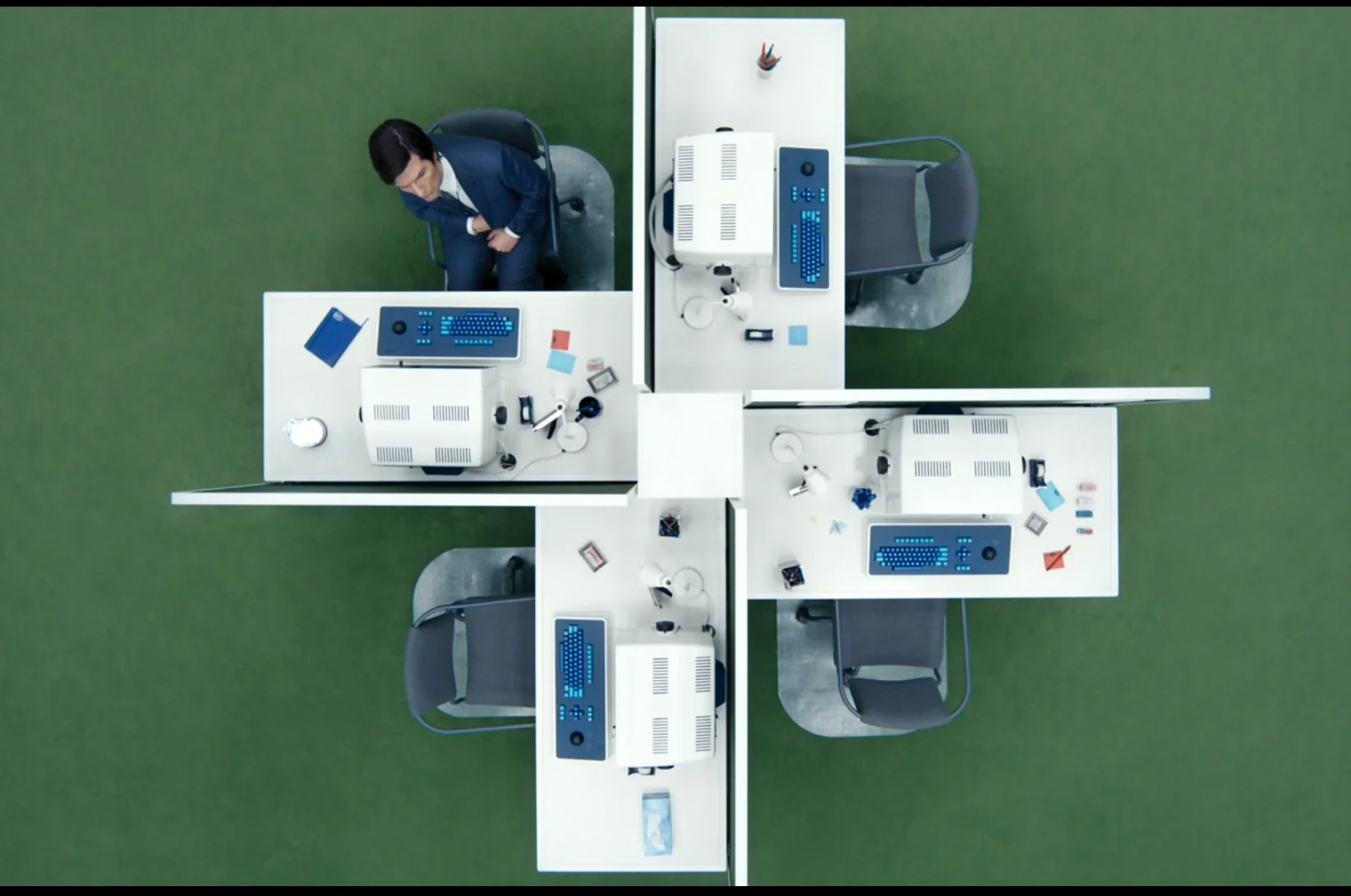 Top-down photo of a cluster of four office desks, all facing in different directions. Three of the four desks are unoccupied.
