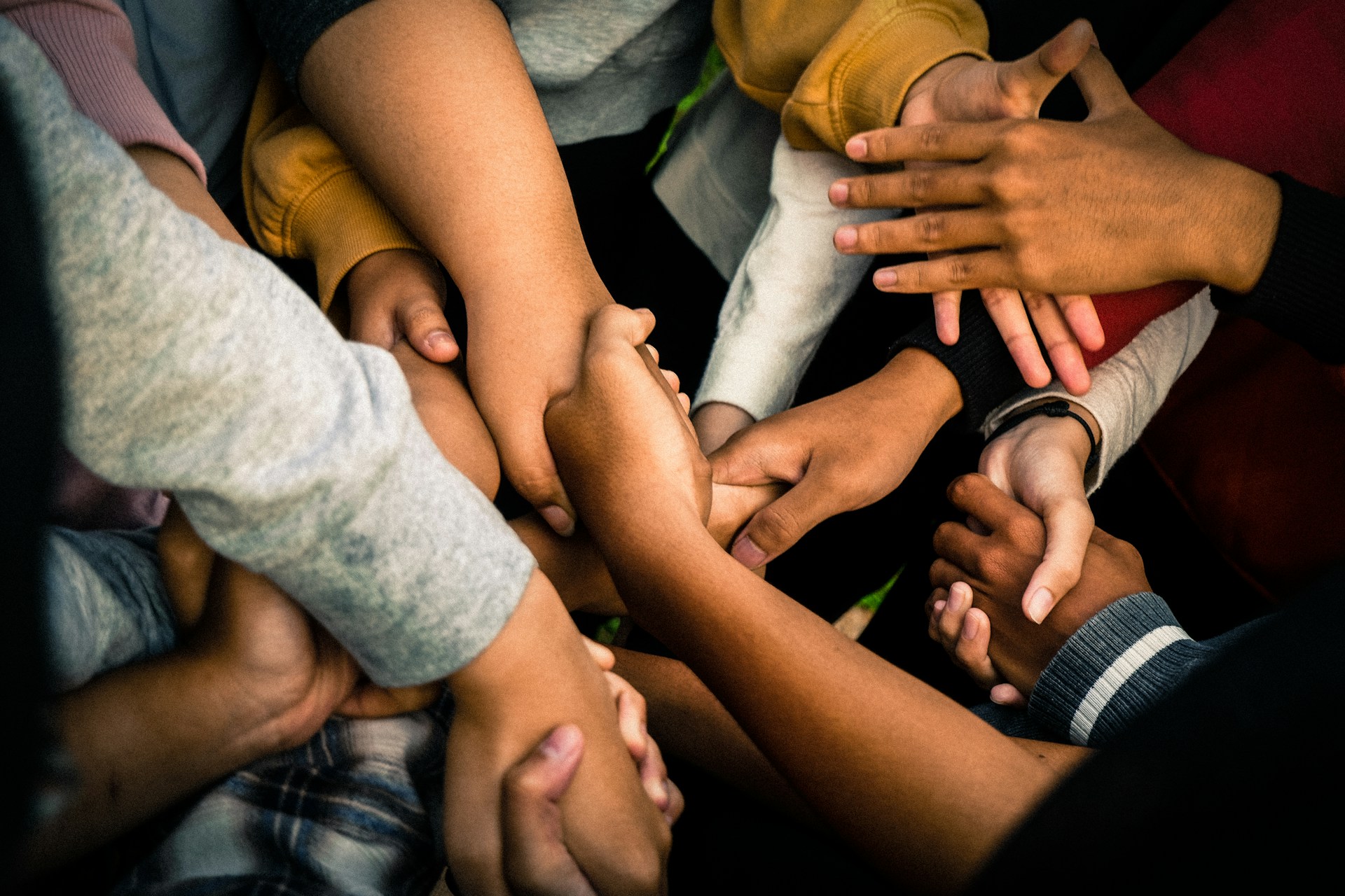 Photo of a large number of arms extended into the center of the frame, many of which are shaking hands as in greeting.